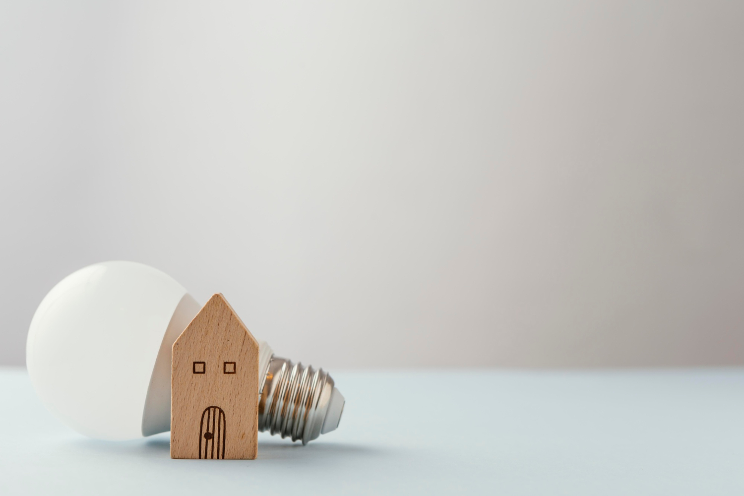 Une ampoule est placée derrière une petite maison en bois pour représenter le concept de maison économe